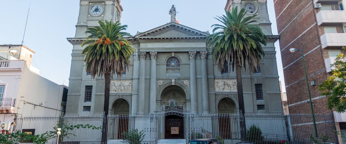 A historic church with two bell towers, a central dome, and palm trees in front.