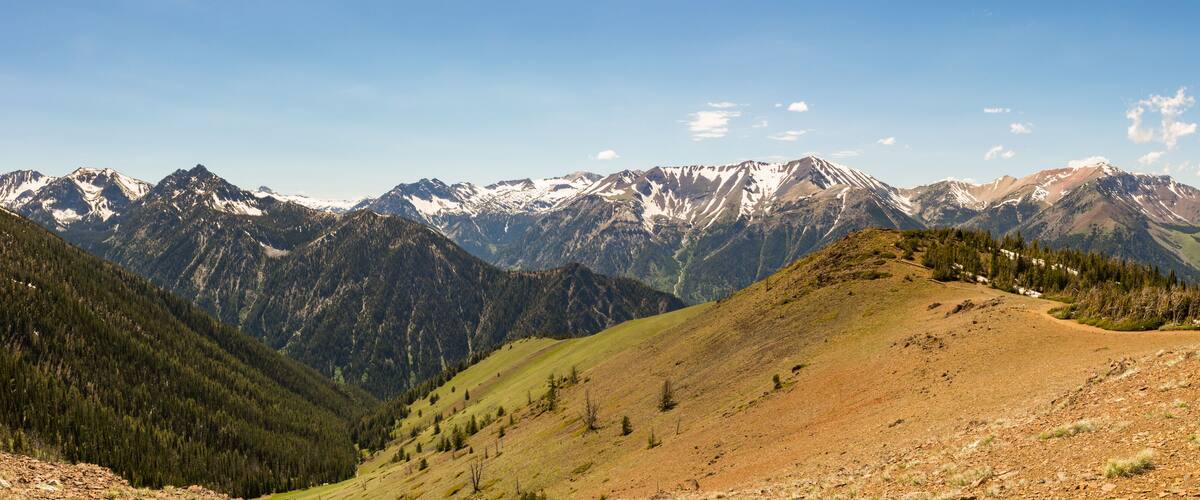 A mountain range with snow-capped peaks, a valley with sparse vegetation, and a clear blue sky.