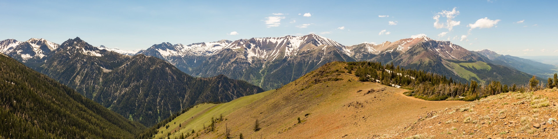 A mountain range with snow-capped peaks, a valley with sparse vegetation, and a clear blue sky.