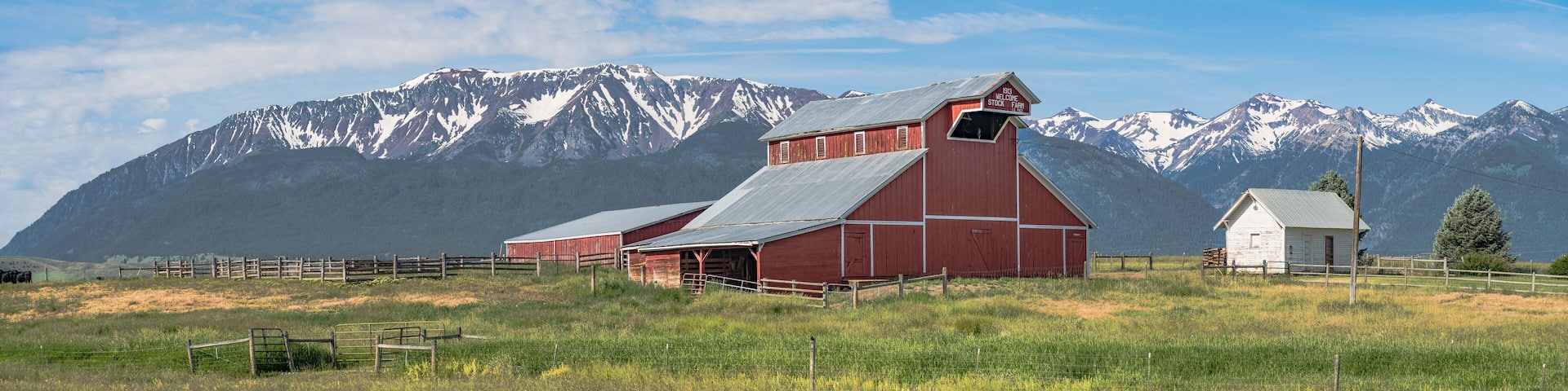 A red barn with a slanted roof, a white building, and a mountainous backdrop.