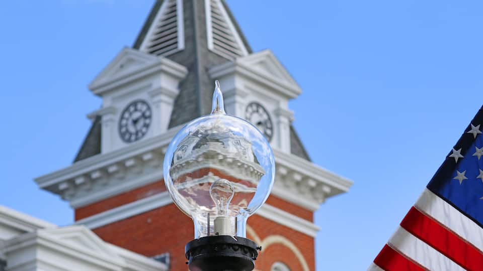 A clear glass globe atop a lamp post, with a clock tower and American flag in the background.