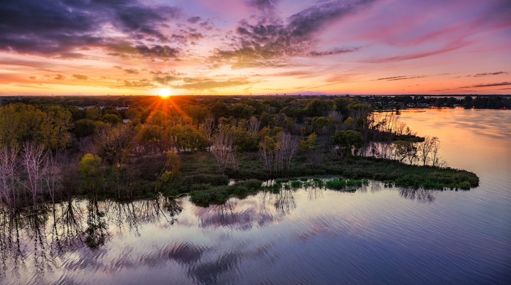 A sunset over a calm lake with trees reflecting the sky, surrounded by a forested area.