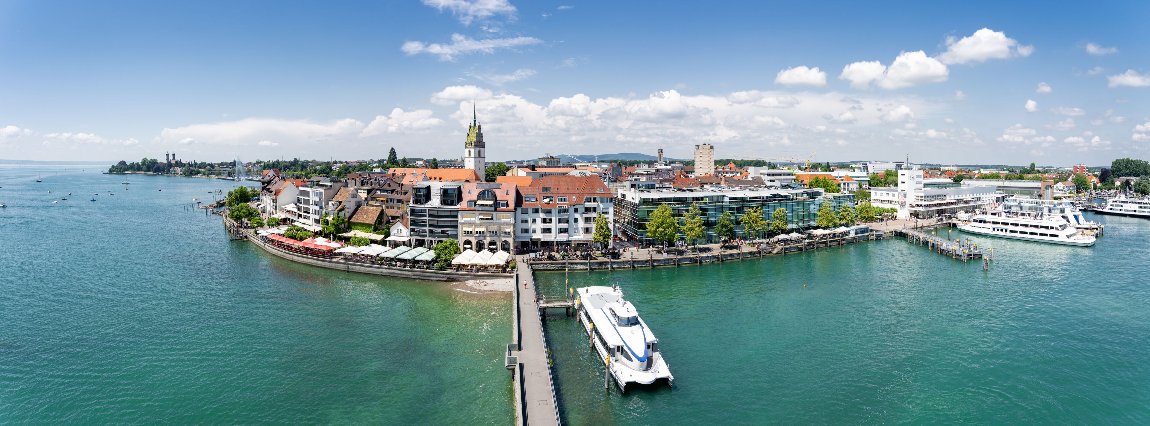 A waterfront cityscape with a prominent church tower, a marina with boats, and a mix of historic and modern buildings.