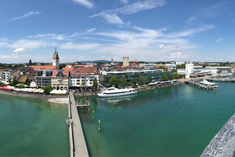 A waterfront cityscape with a prominent church steeple, a modern glass building, and a marina with boats.