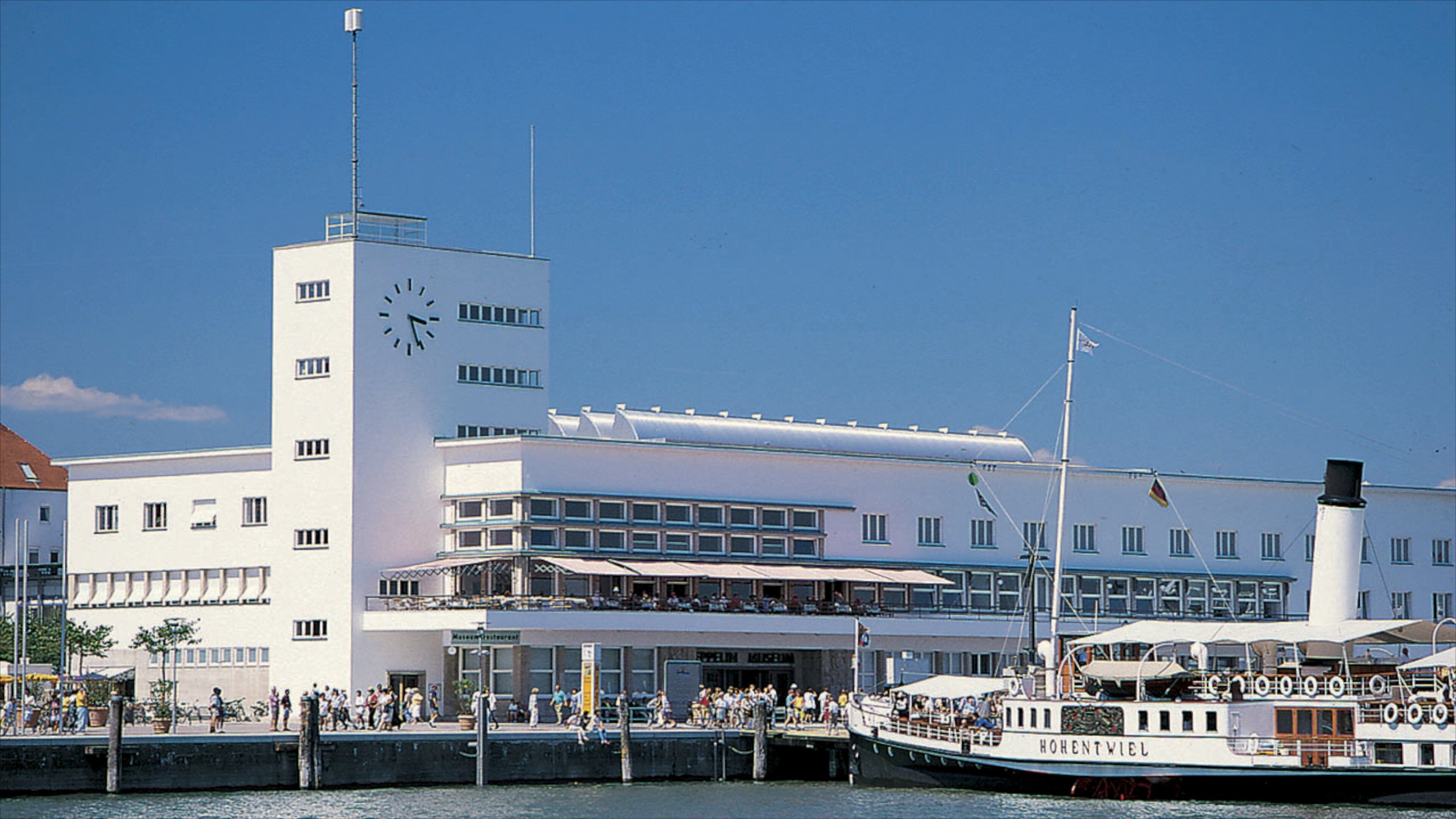 A white building with a clock tower, a museum, and a boat docked at the waterfront.