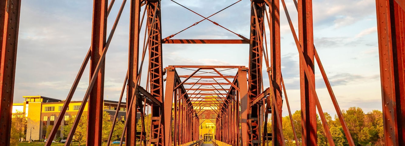 Un puente peatonal de madera con estructura de celosía metálica.