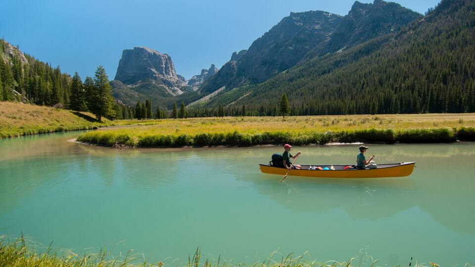 A calm river with a canoe, surrounded by mountains and dense forests.
