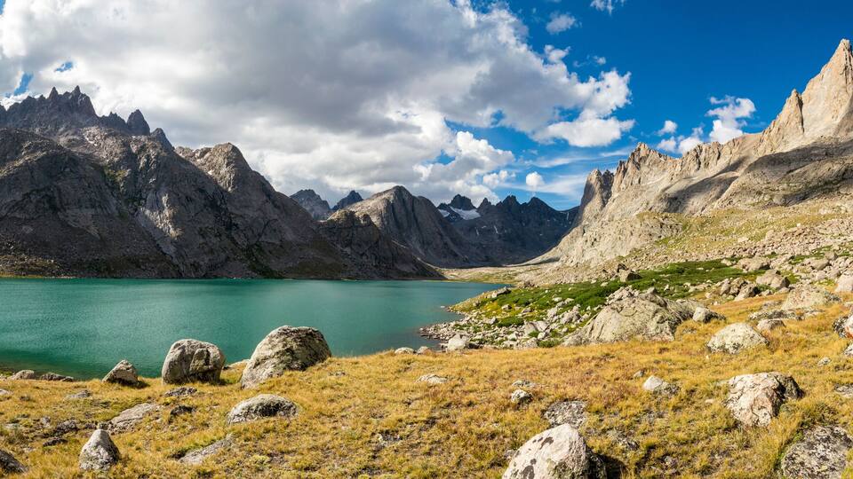 A mountainous landscape with a turquoise lake surrounded by rocky terrain and sparse grass.