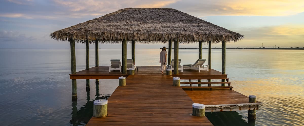 Un muelle de madera que lleva a una construcción de techo de paja sobre aguas tranquilas.