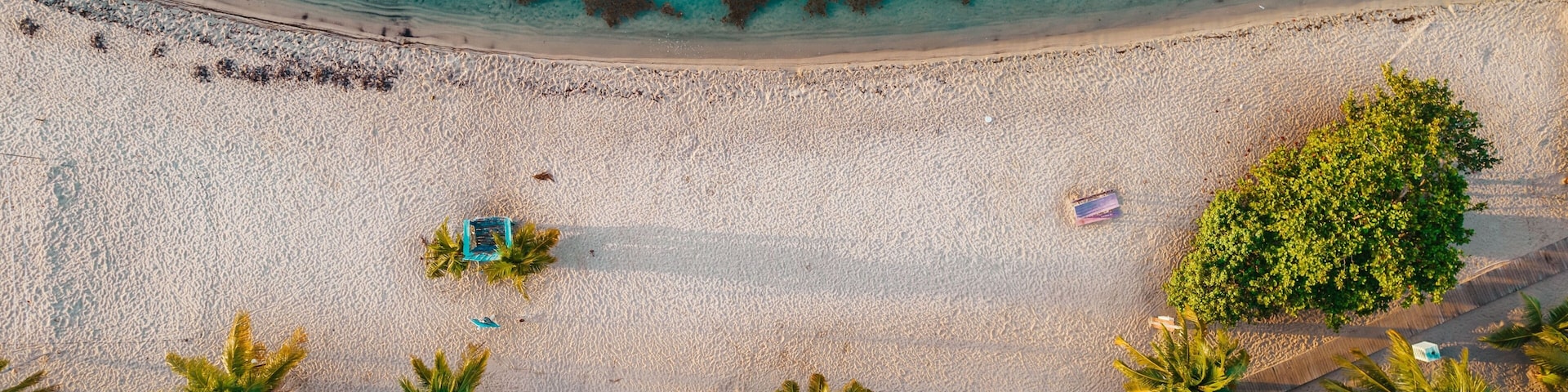 A beach with clear turquoise water, palm trees, and a lifeguard tower.