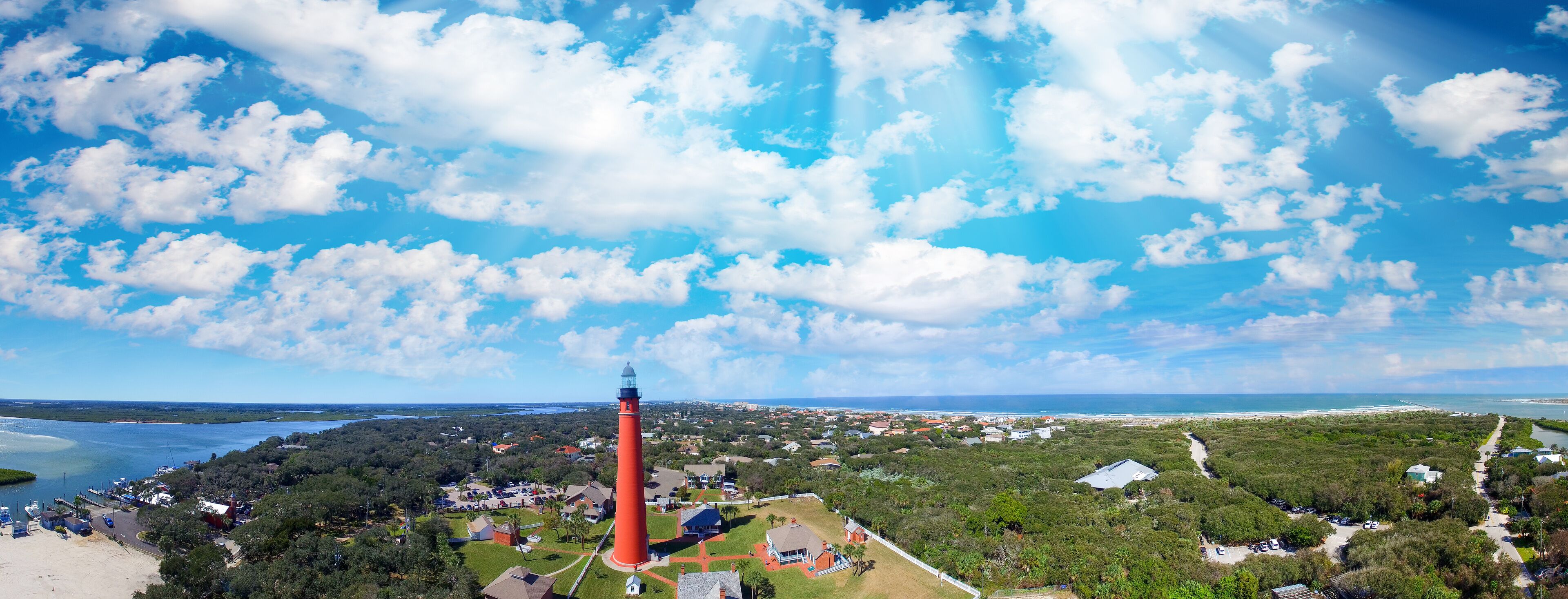 A coastal town with a prominent red lighthouse, a marina, and a mix of residential and commercial buildings.