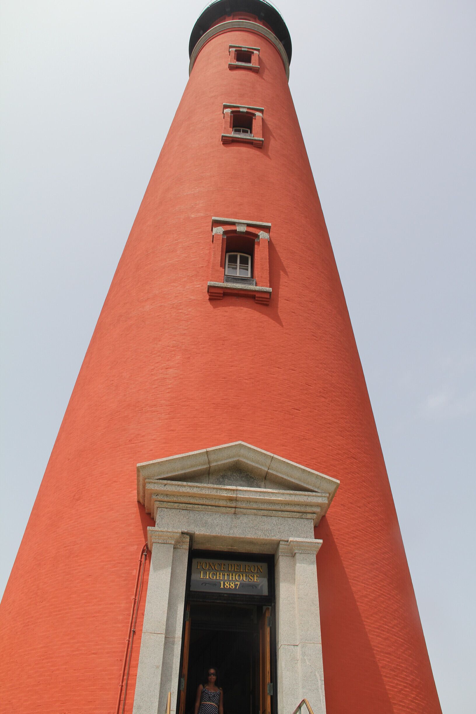 A tall red lighthouse with a plaque reading "FONCE DELON LIGHTHOUSE 1887" at the base.