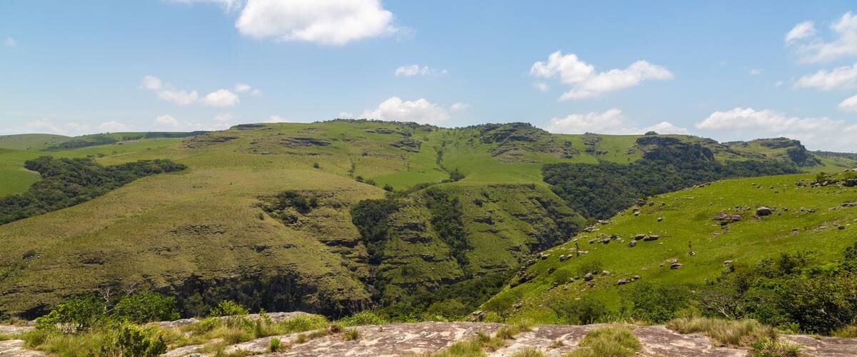 Rolling green hills with a valley and scattered rocks.