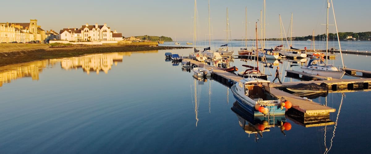 A marina with boats docked, a calm water body, and buildings in the background.