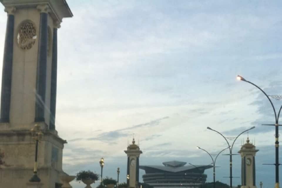 A road with a monument on the left and a modern building in the distance.