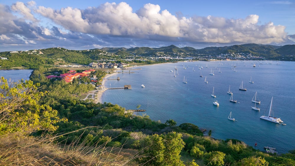 Un paysage côtier avec des voiliers, une plage et une ville en arrière-plan.