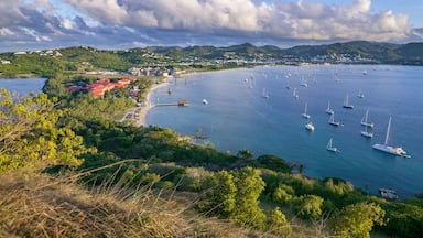 Un paisaje costero con veleros, una playa y un pueblo al fondo.