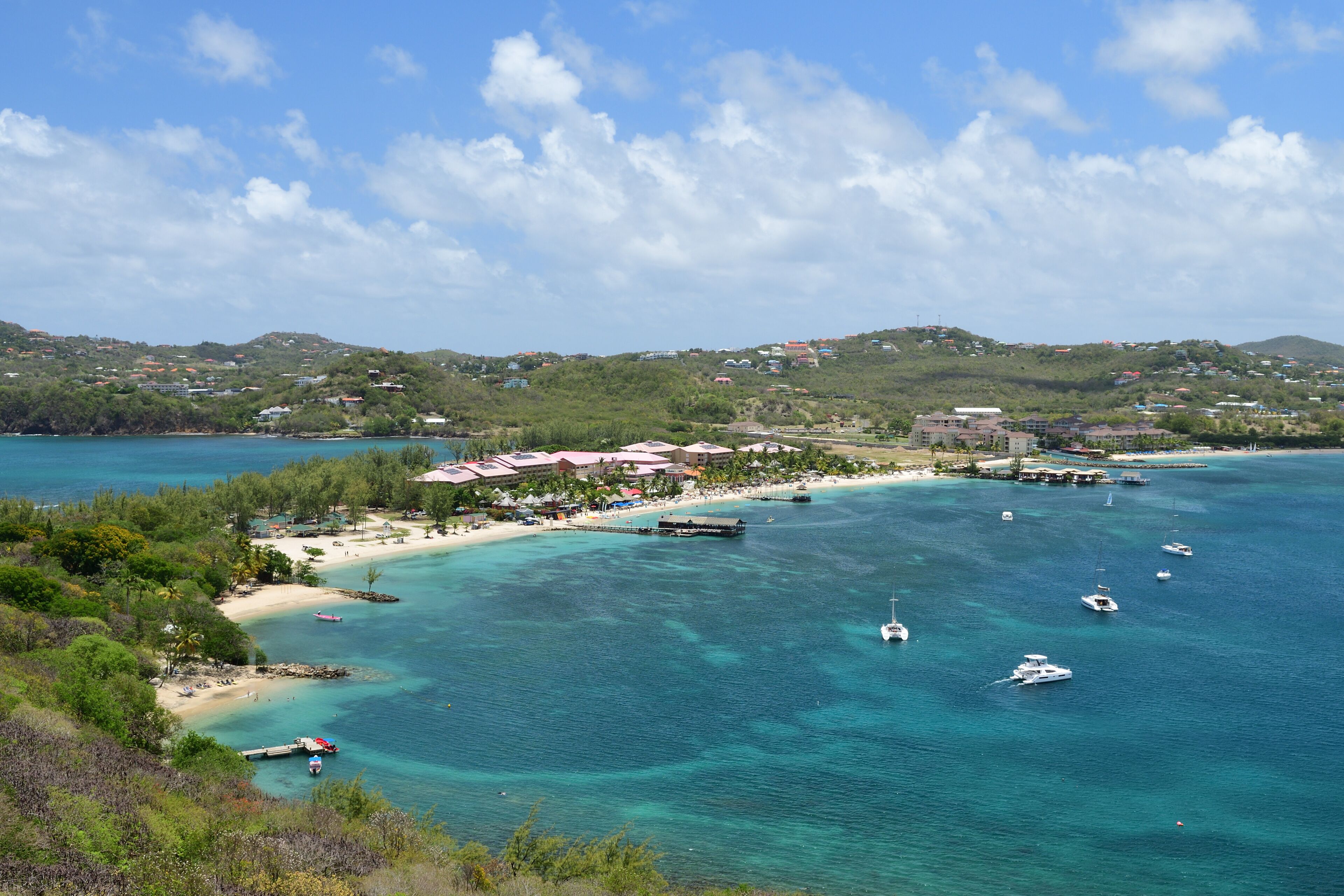 A coastal town with a beach, clear turquoise waters, boats, and a hilly backdrop.