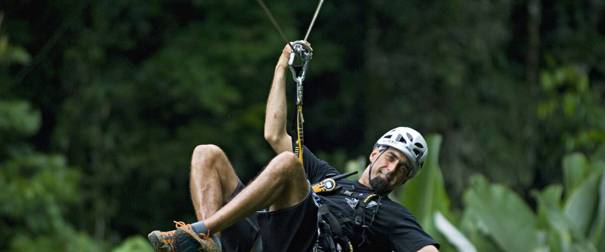 A person zip-lining through a dense forest.