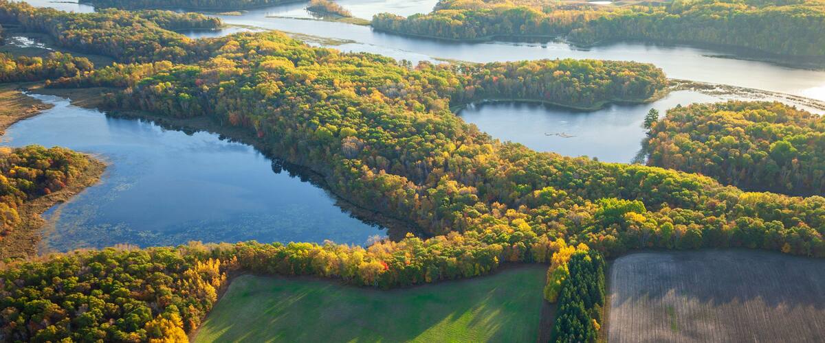 An aerial view of a river system with surrounding forested areas and patches of open fields.