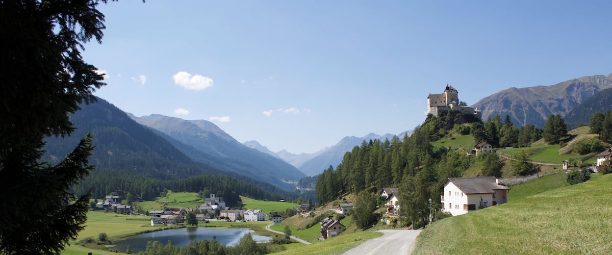 Ländliche Landschaft mit Feldweg, See, Häusern und Burg auf einem Hügel.