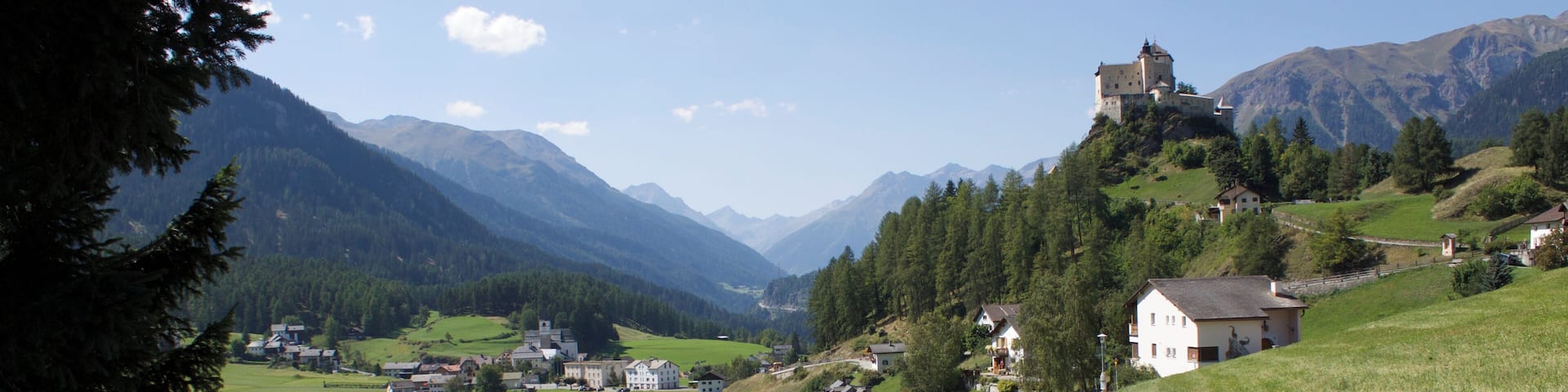 A rural landscape with a dirt road, a lake, houses, and a castle on a hill.