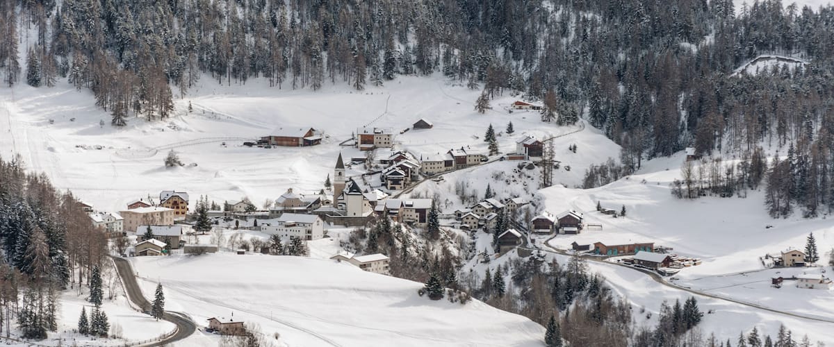 A snow-covered village nestled in a mountainous area with dense forests.