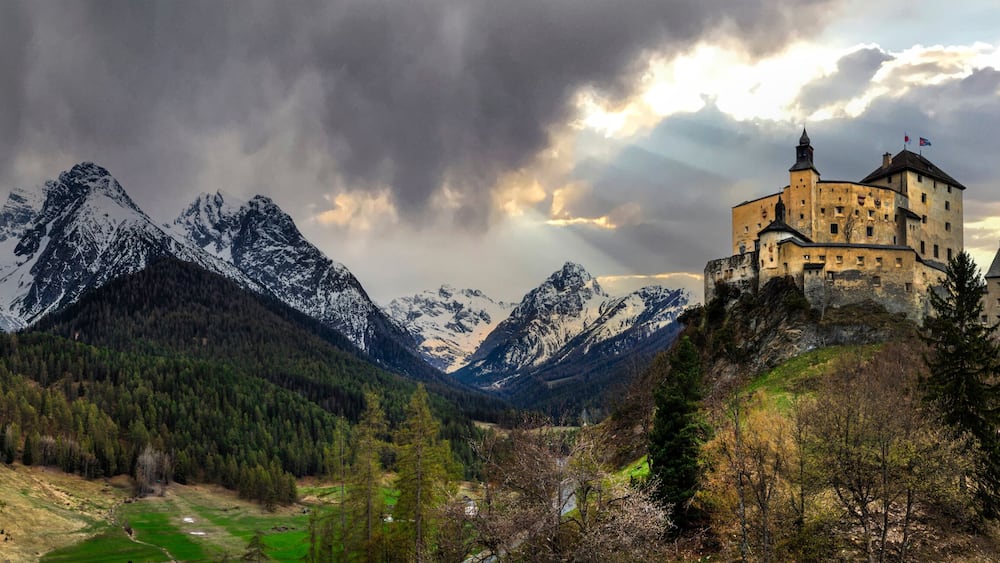 Un chùteau perché sur une colline, avec des montagnes enneigées en arriÚre-plan.