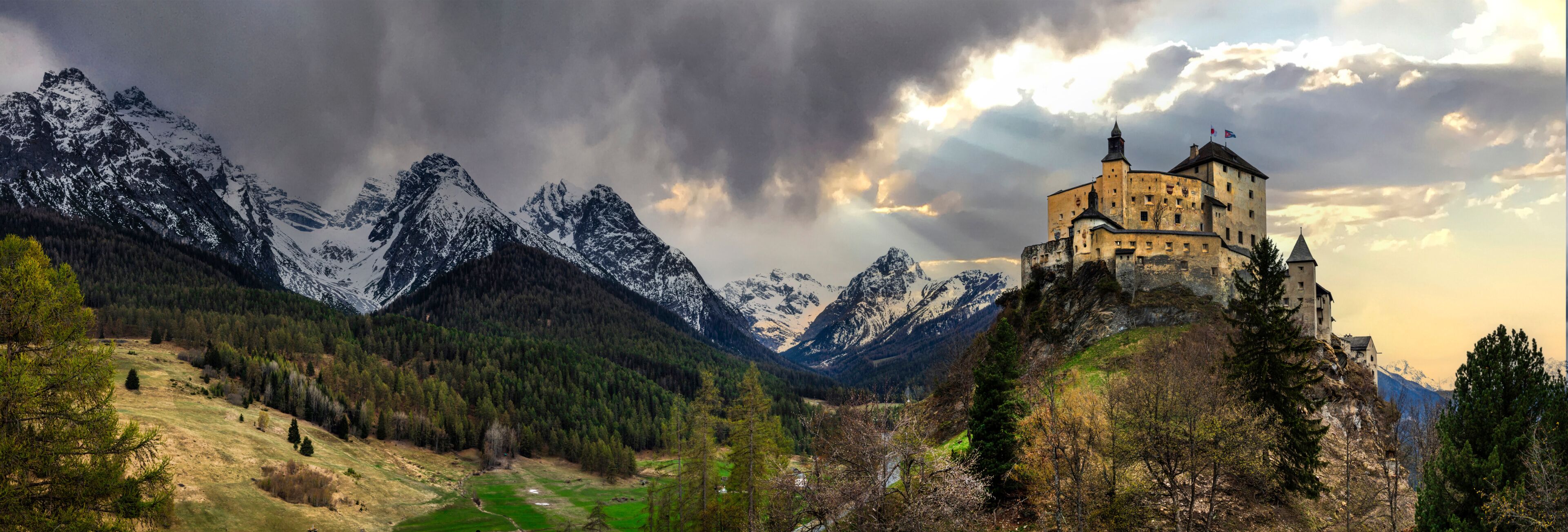 A castle on a hill with snow-capped mountains in the background.