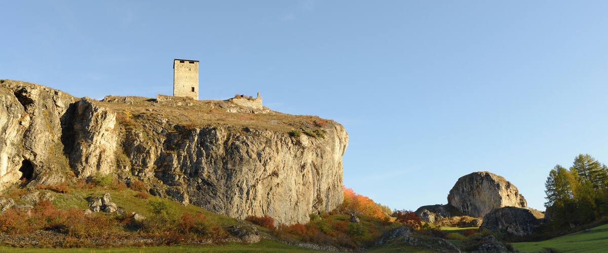 A castle on a rocky cliff with a grassy field in the foreground.