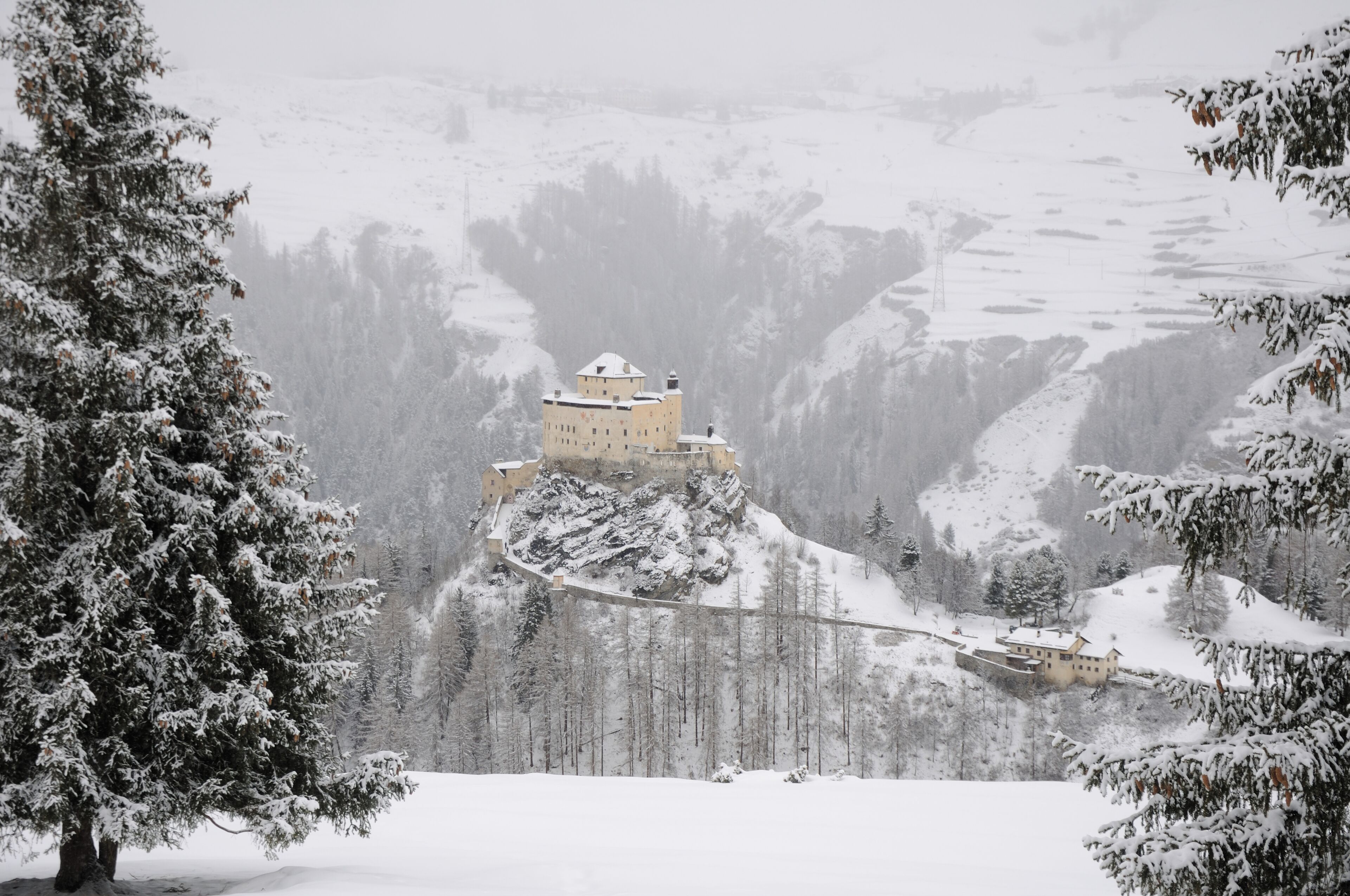 A snow-covered castle on a hill with a forested valley in the background.