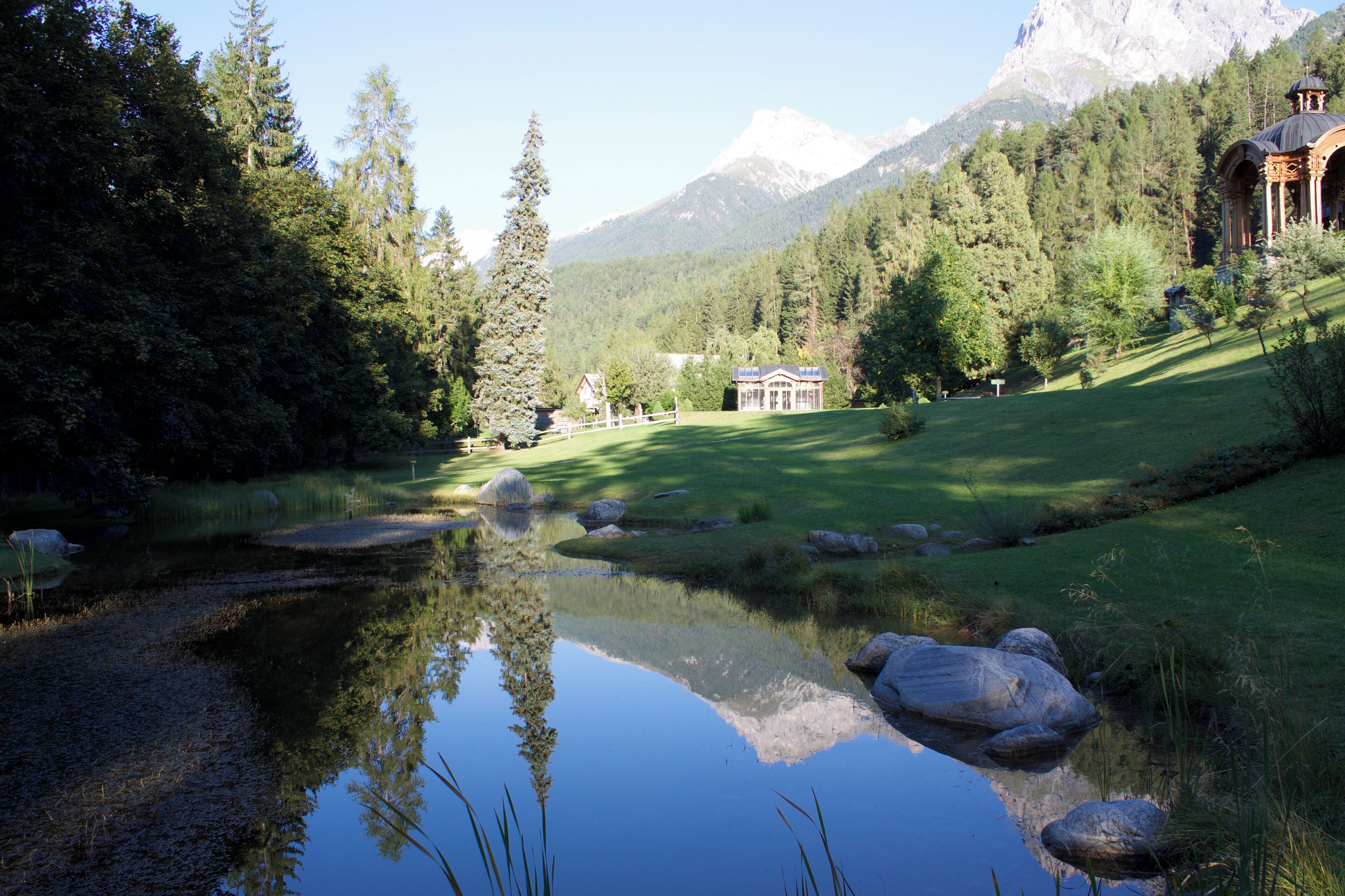 A serene lake with reflections, surrounded by lush greenery and mountains in the background.