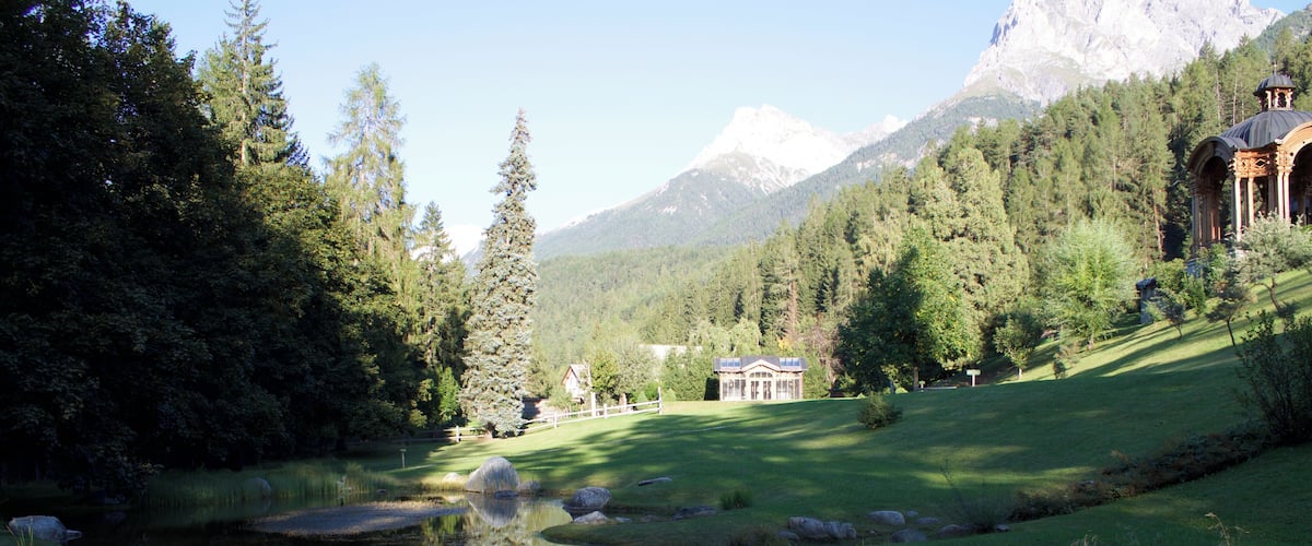 A serene lake with reflections, surrounded by lush greenery and mountains in the background.