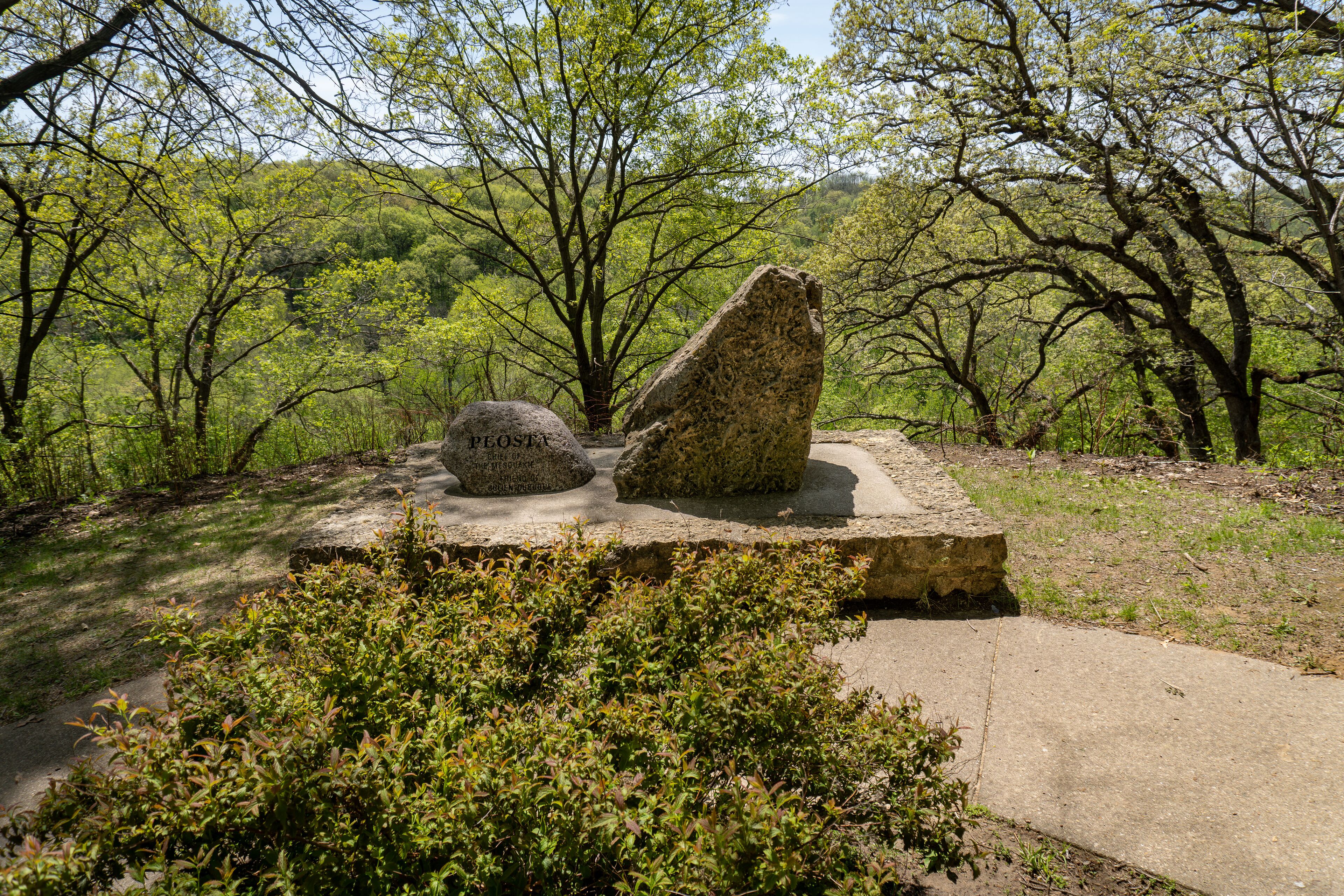 A stone monument with inscriptions in a natural setting surrounded by trees and greenery.