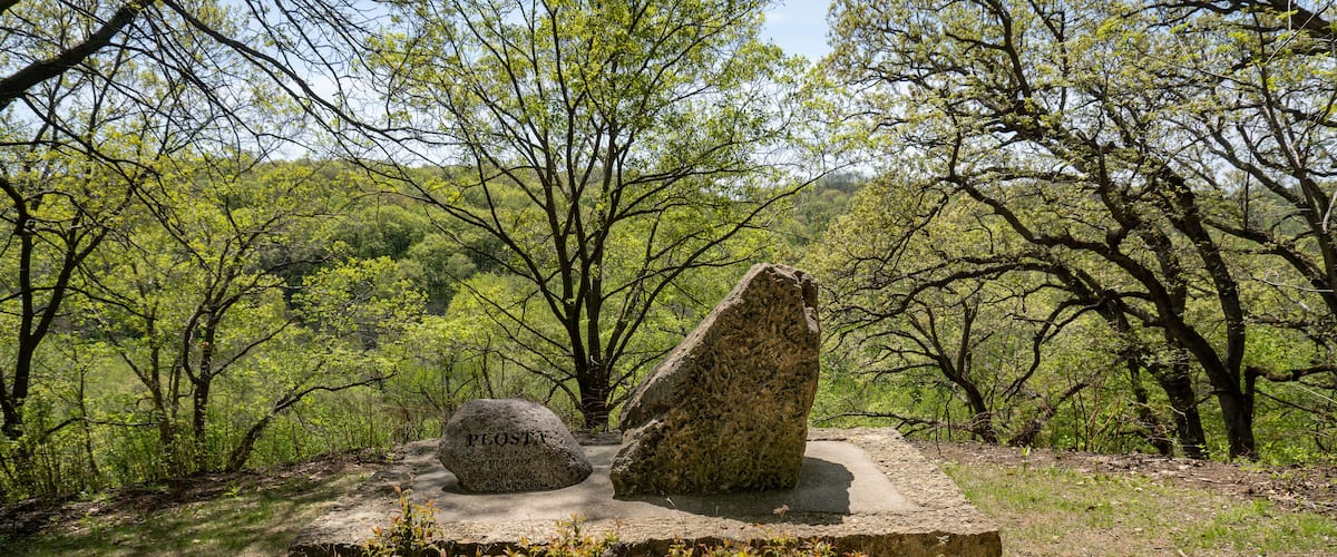 A stone monument with inscriptions in a natural setting surrounded by trees and greenery.
