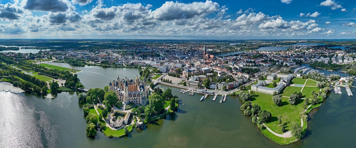 An aerial view of a city with a river, a castle, and surrounding greenery.