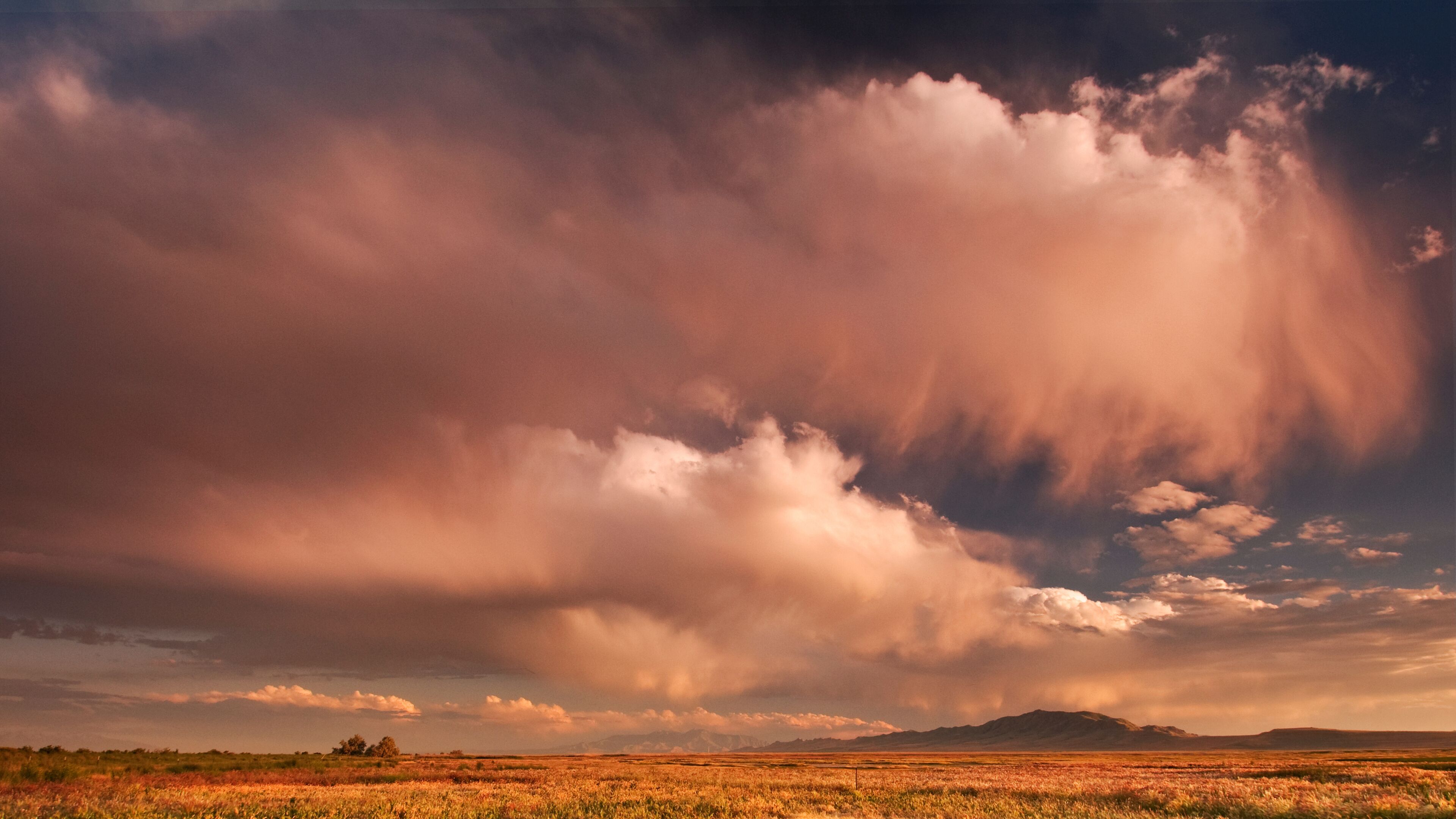 A vast landscape with a dramatic sky, featuring a field and distant mountains.