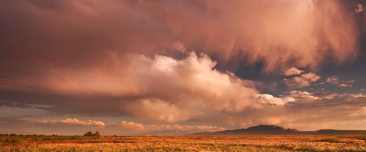 A vast landscape with a dramatic sky, featuring a field and distant mountains.