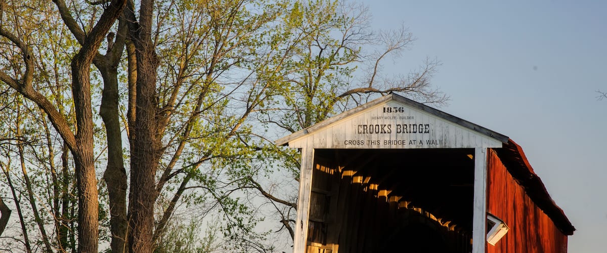 A covered bridge with the inscription "1856 Crooks Bridge" and "Cross this bridge at a wall."