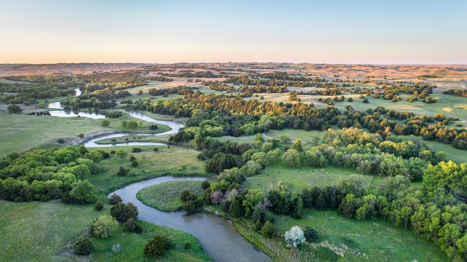A river winding through a lush green landscape with dense trees and rolling hills.