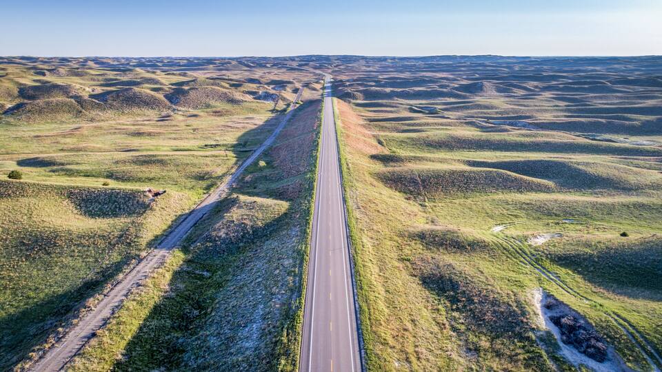 A long straight road cutting through rolling hills.