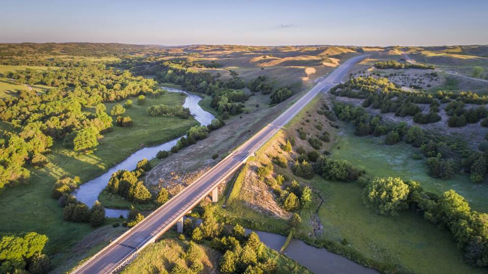 A river running alongside a highway through a green landscape with hills.