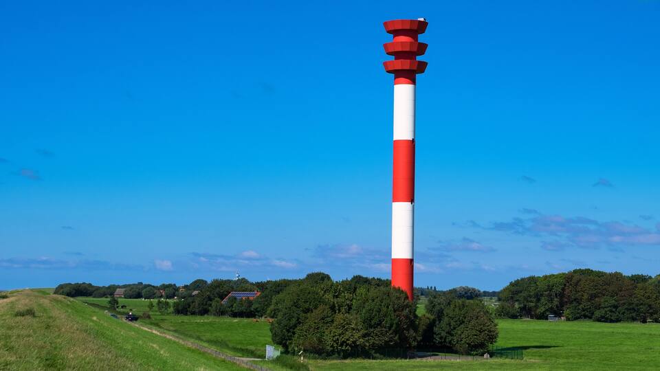 A red and white lighthouse on a grassy hill with a clear blue sky.