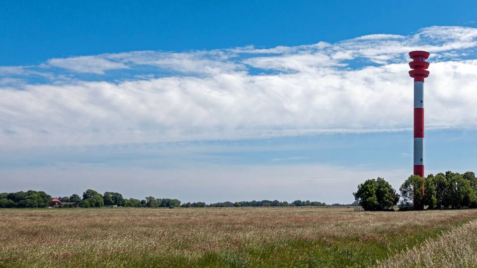 A red and white lighthouse in a field with a clear blue sky and scattered clouds.