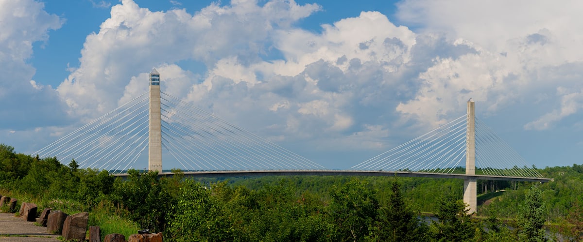 A cable-stayed bridge with tall towers, surrounded by lush greenery and a partly cloudy sky.