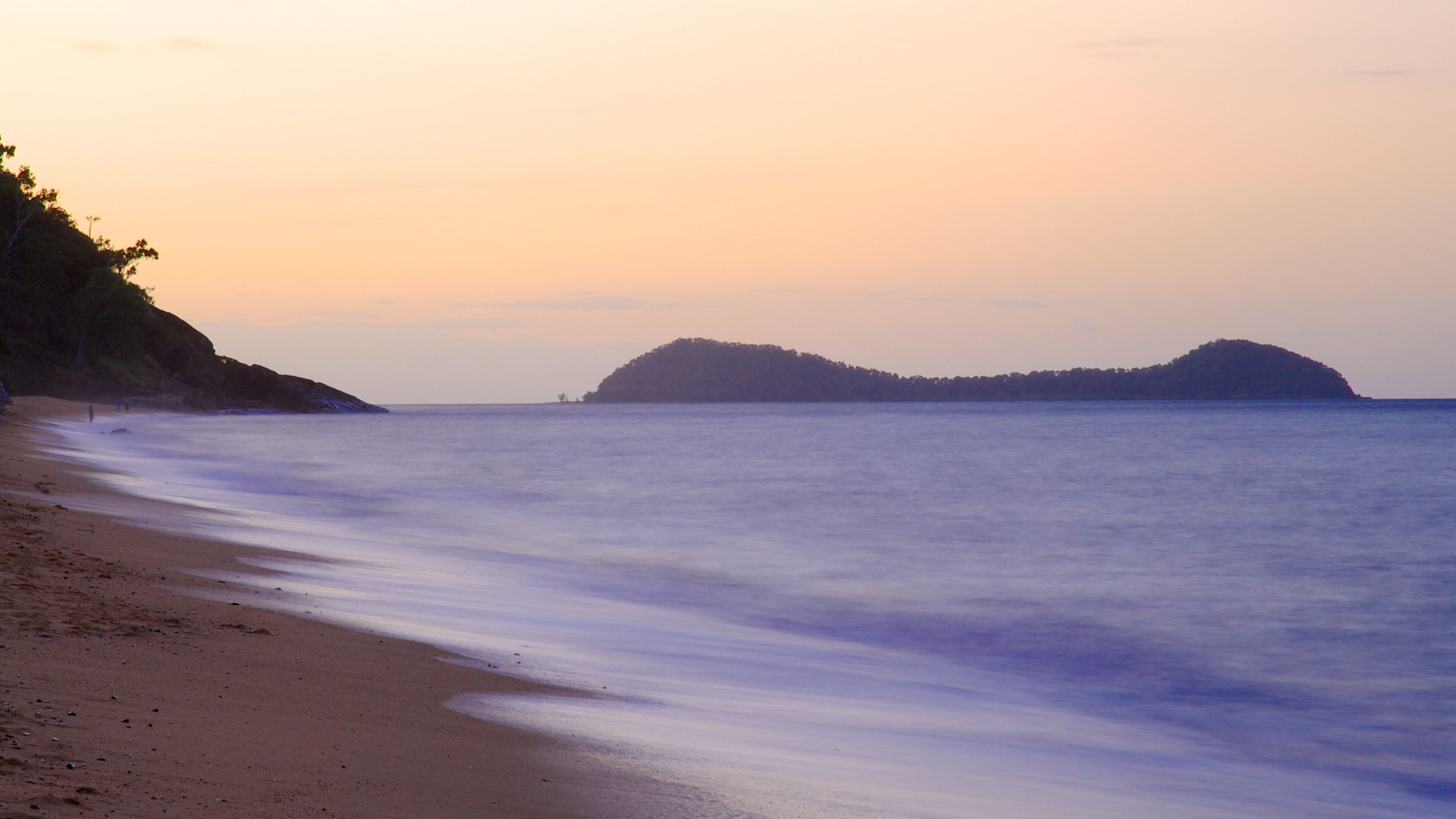 Una playa con aguas tranquilas y una isla distante.
