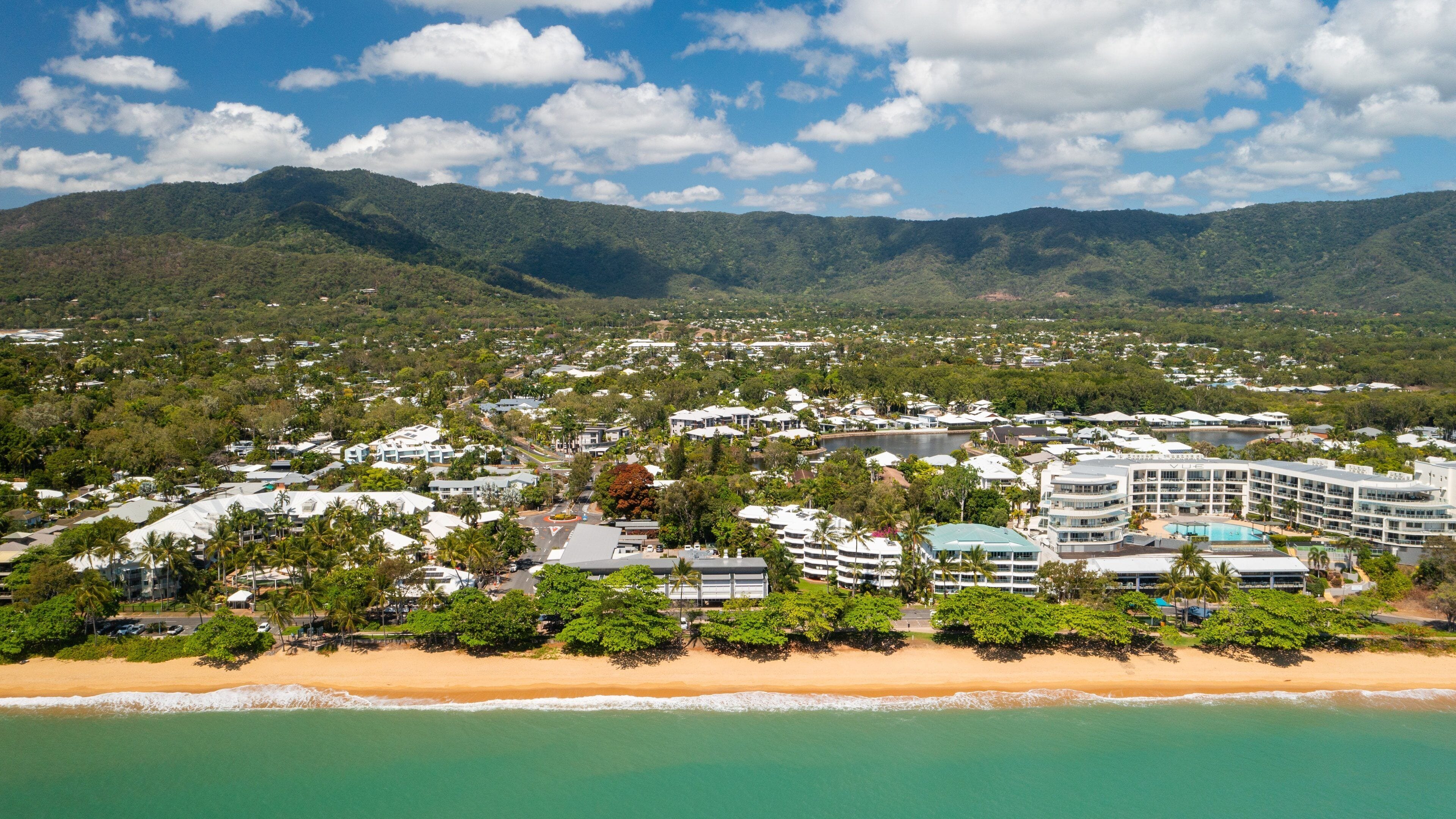 Un pueblo costero con playa, edificios residenciales y montañas al fondo.