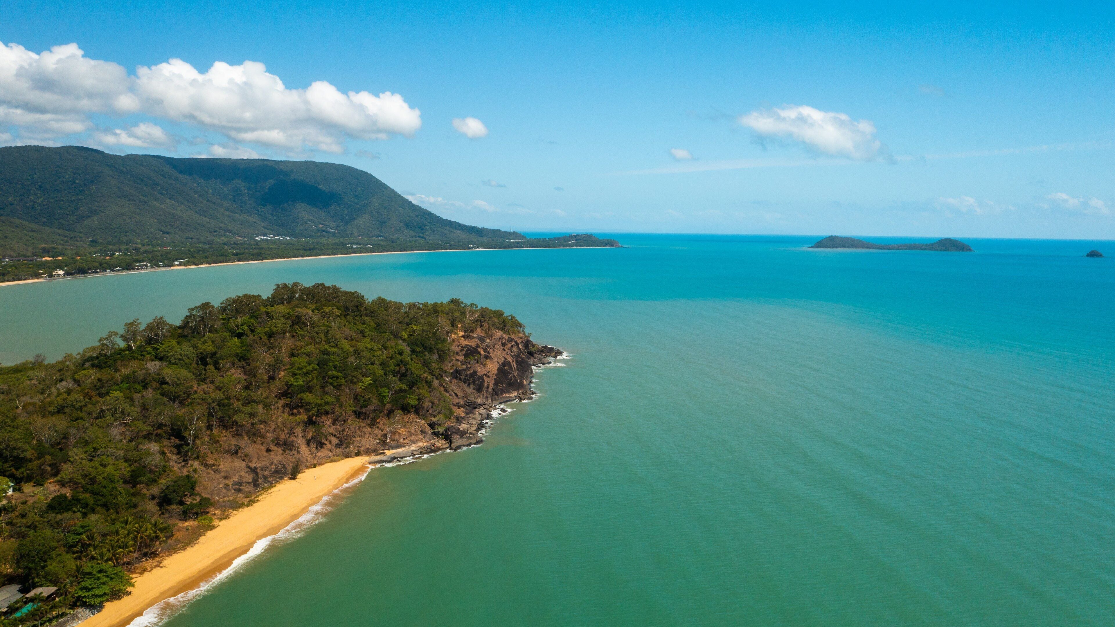 A coastal landscape with a sandy beach, clear turquoise waters, and a forested island.