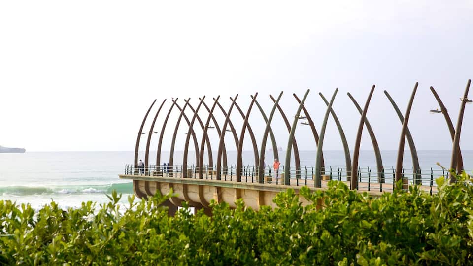 A coastal walkway with a series of curved metal structures, a bridge, and the ocean in the background.
