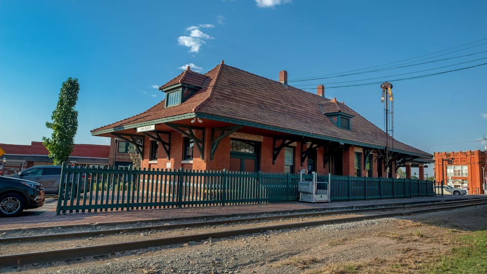 Ein Bahnhof im Vintage-Stil mit rotem Dach, grüner Umzäunung und blauem Himmel.